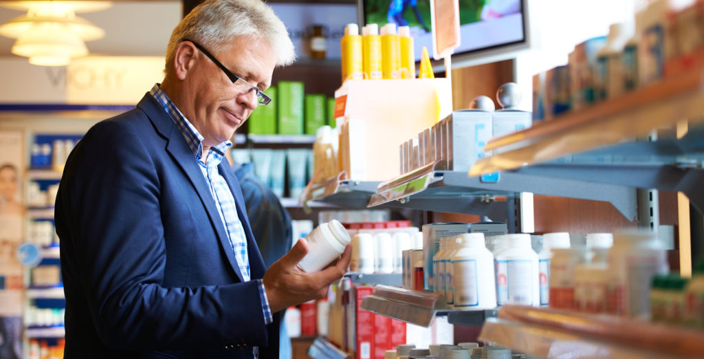 Older man selecting medication from a store shelf.
