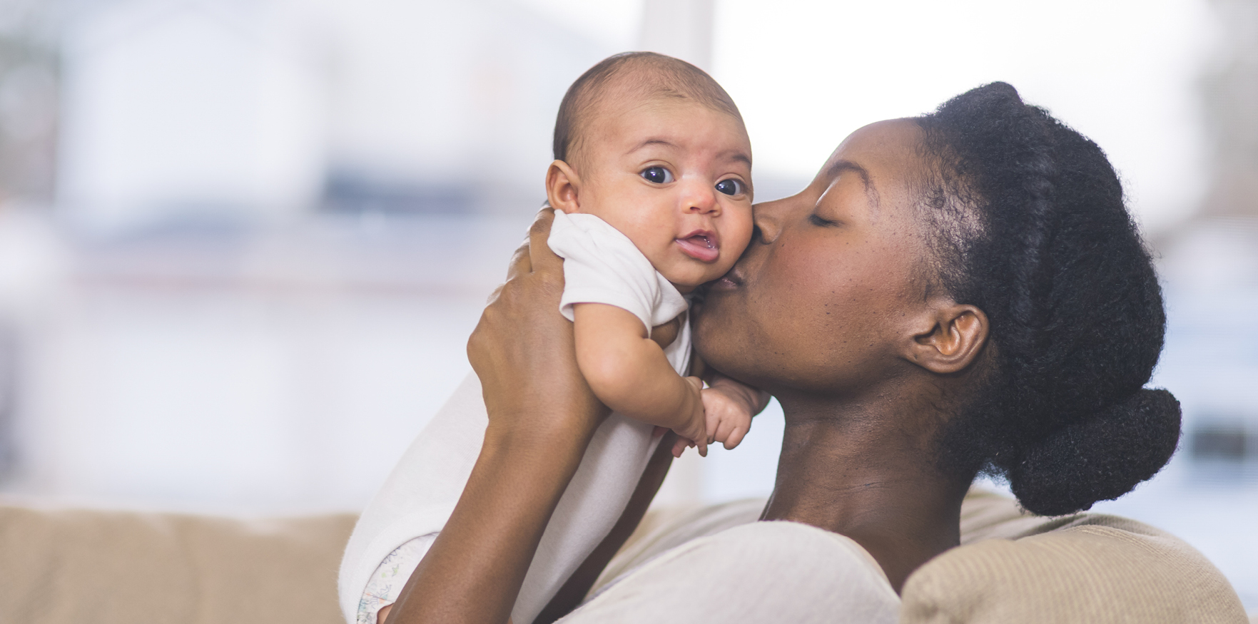 mom holding up baby and kissing it on the cheek