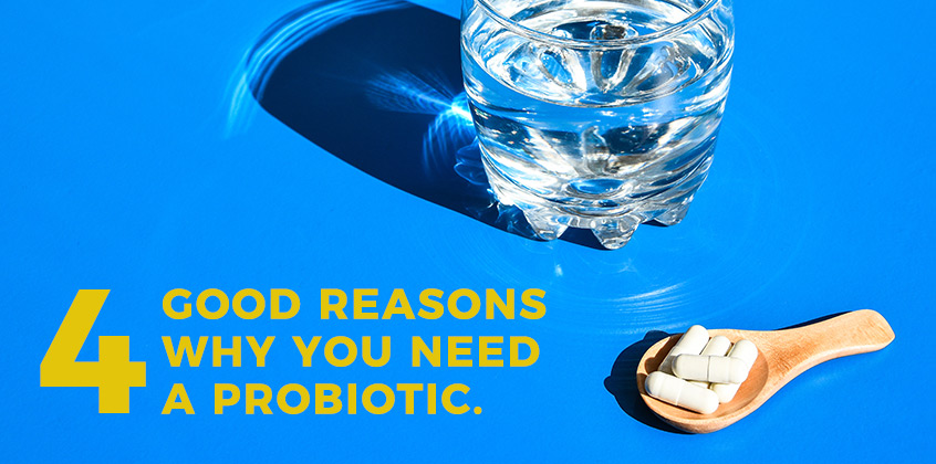 Five capsules on a wooden measuring spoon next to a glass of water. Text: 4 Good reasons why you need a probiotic