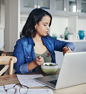 Woman working remotely and eating veggies while checking the time on her watch