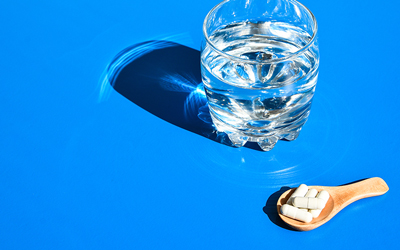 Glass of water next to five capsules. Text: 4 Good Reasons Why You Need A Probiotic