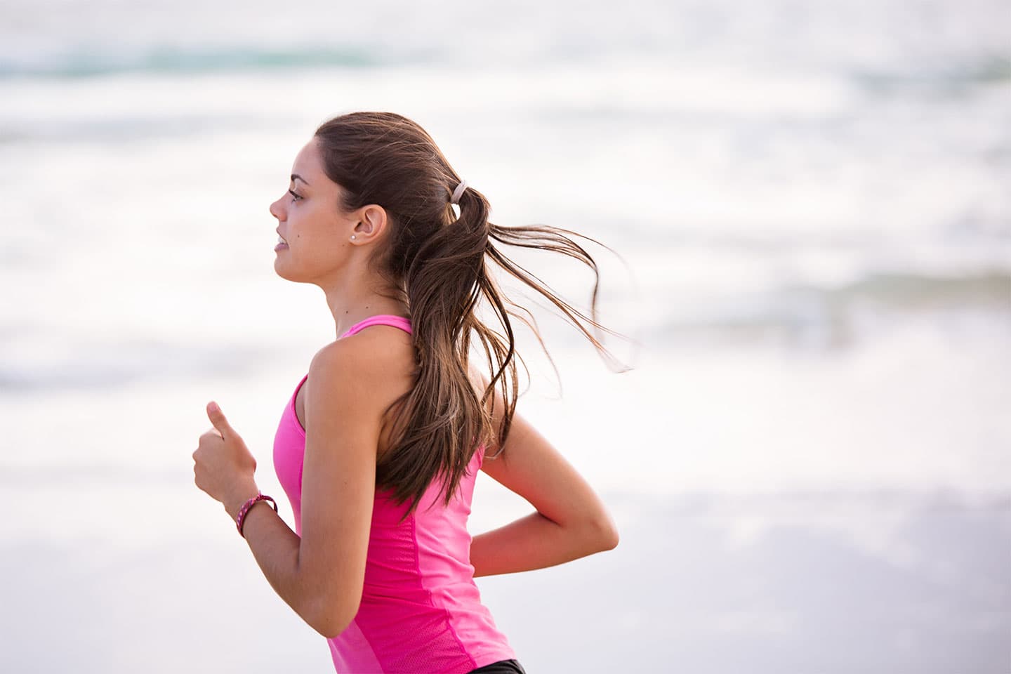 Woman with pony tail in pink tank top running on beach shore