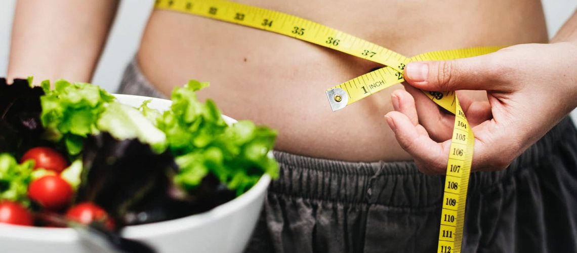 a woman holding a salad and measuring her waist
